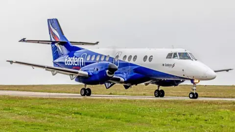 A blue and white plane taxiing on a runway.